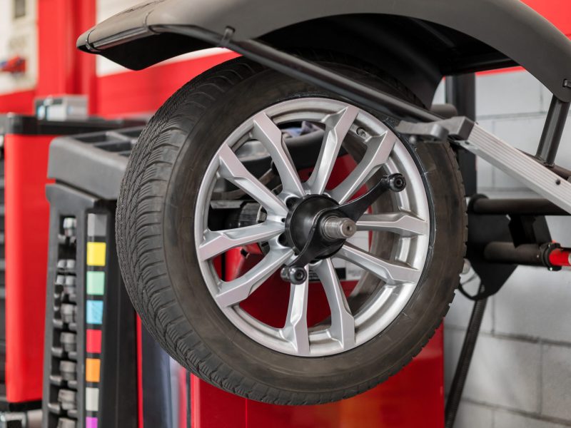 Wheel hanging on wheel balancer during car service inside of modern car dealer shop